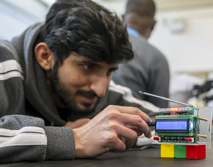 Student closely examining a custom-built radio circuit board with LED indicators and an antenna in an electronics lab Student closely examining a custom-built radio circuit board with LED indicators and an antenna in an electronics lab